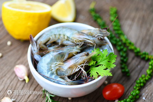 白碗新鲜虾和木制底配有食用海产品生虾的饲料草药和香